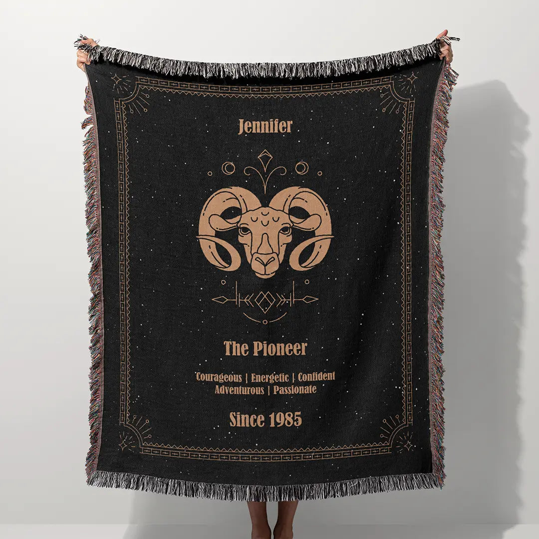 A custom blanket featuring an Aries zodiac design held up on a white background, showcasing a personalized name, date, and traits.