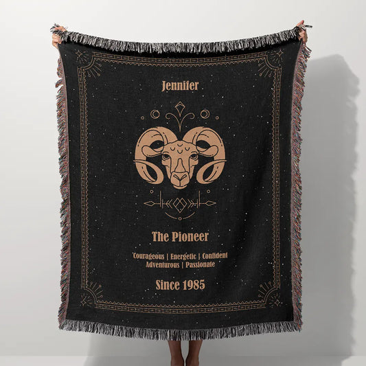 A custom blanket featuring an Aries zodiac design held up on a white background, showcasing a personalized name, date, and traits.