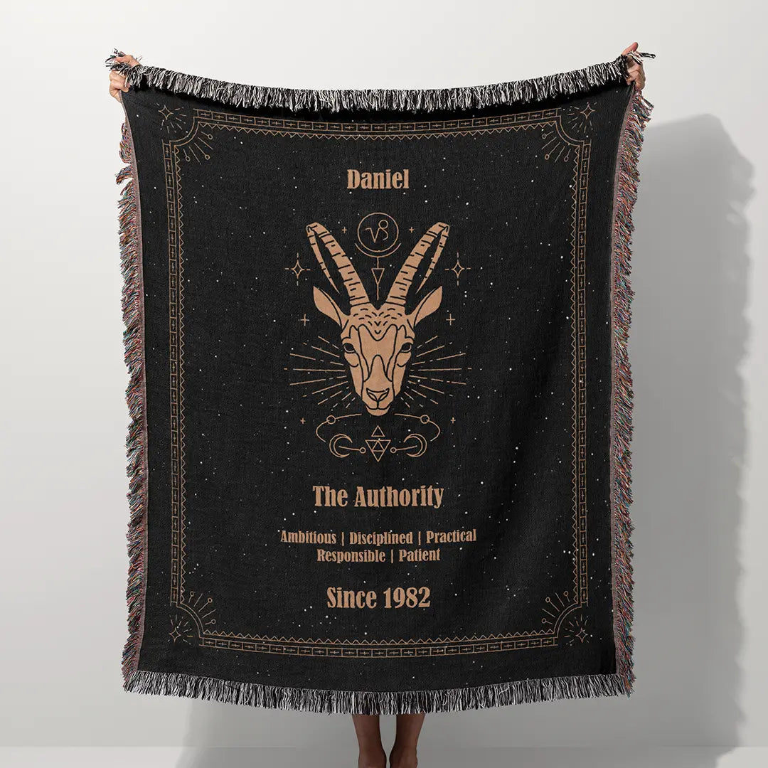 A custom blanket featuring a Capricorn zodiac design held up on a white background, showcasing a personalized name, date, and traits.