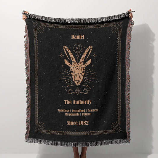 A custom blanket featuring a Capricorn zodiac design held up on a white background, showcasing a personalized name, date, and traits.