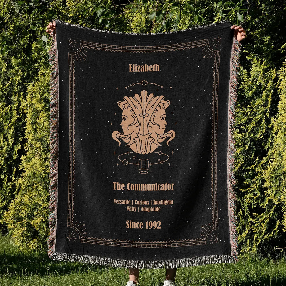 Custom woven cotton blanket featuring a Gemini zodiac design, held up outdoors against vibrant green foliage.