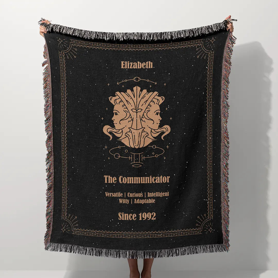 A custom blanket featuring a Gemini zodiac design held up on a white background, showcasing a personalized name, date, and traits.