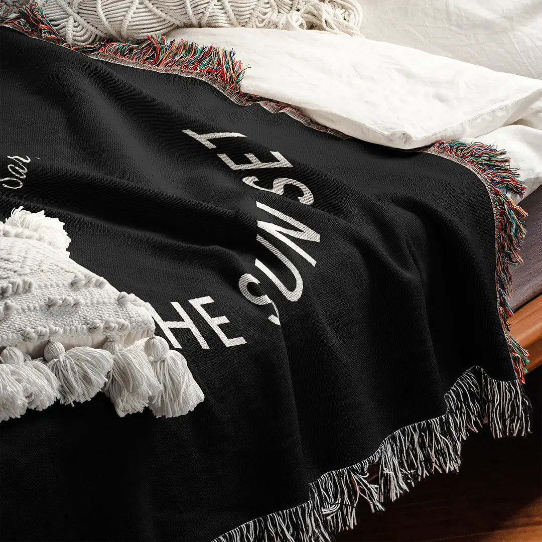 A close-up of a custom woven cotton name blanket for couples on a bed, showing the soft texture, woven white typography, and detailed multicolor fringe edges.
