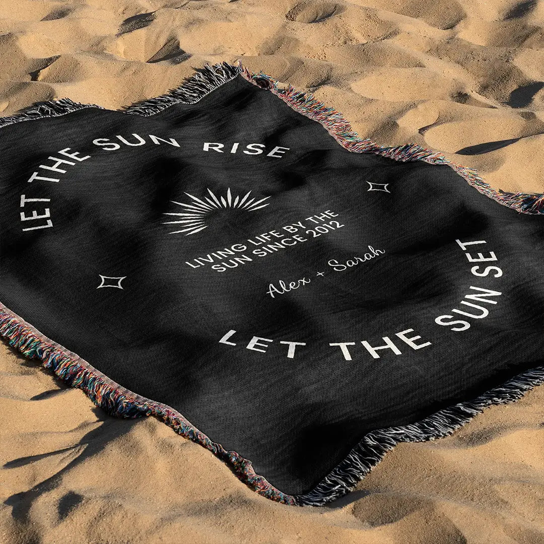 A custom woven cotton name blanket for couples with a quote and personalization text options, laid out on the sand, styled as a beach throw.