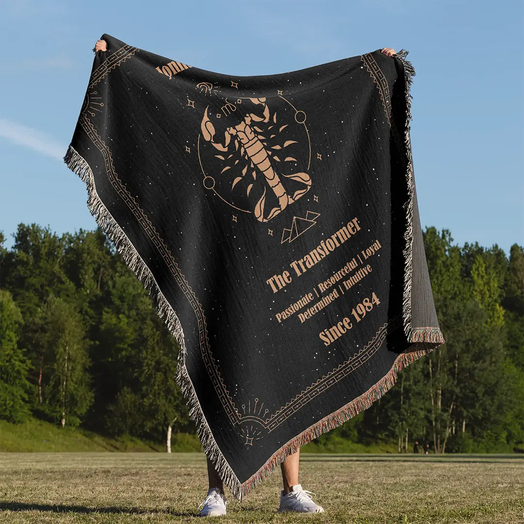 Man holding up a custom woven cotton blanket featuring a Scorpio zodiac design with a custom name and traits, set against a forest background.
