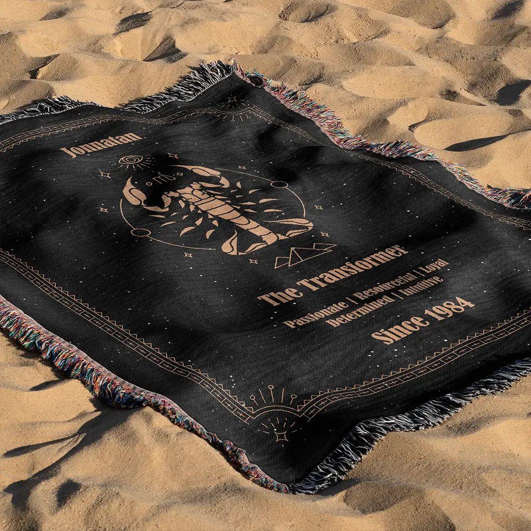 Scorpio-themed custom woven cotton blanket laid out on sandy beach terrain, displaying its bold zodiac scorpion symbol.
