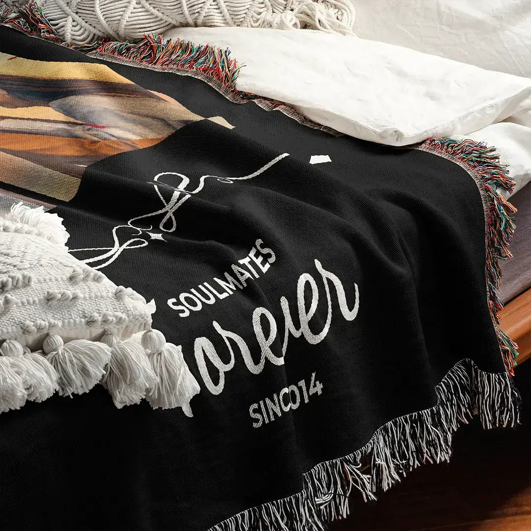 Personalized black woven photo cotton blanket for couples with fringed edges displayed on a bed with white pillows and boho-style cushions.