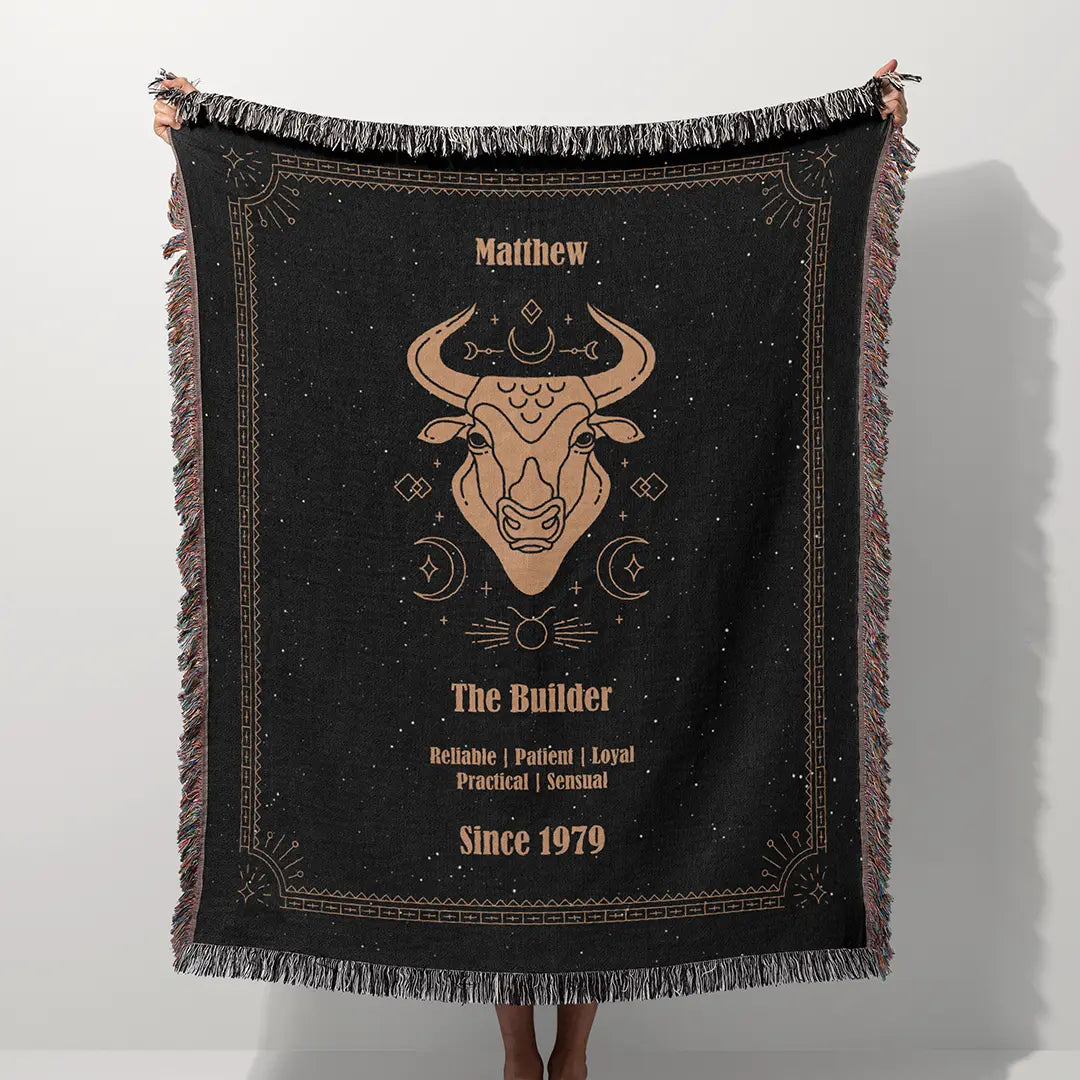 A custom blanket featuring a Taurus zodiac design held up on a white background, showcasing a personalized name, date, and traits.