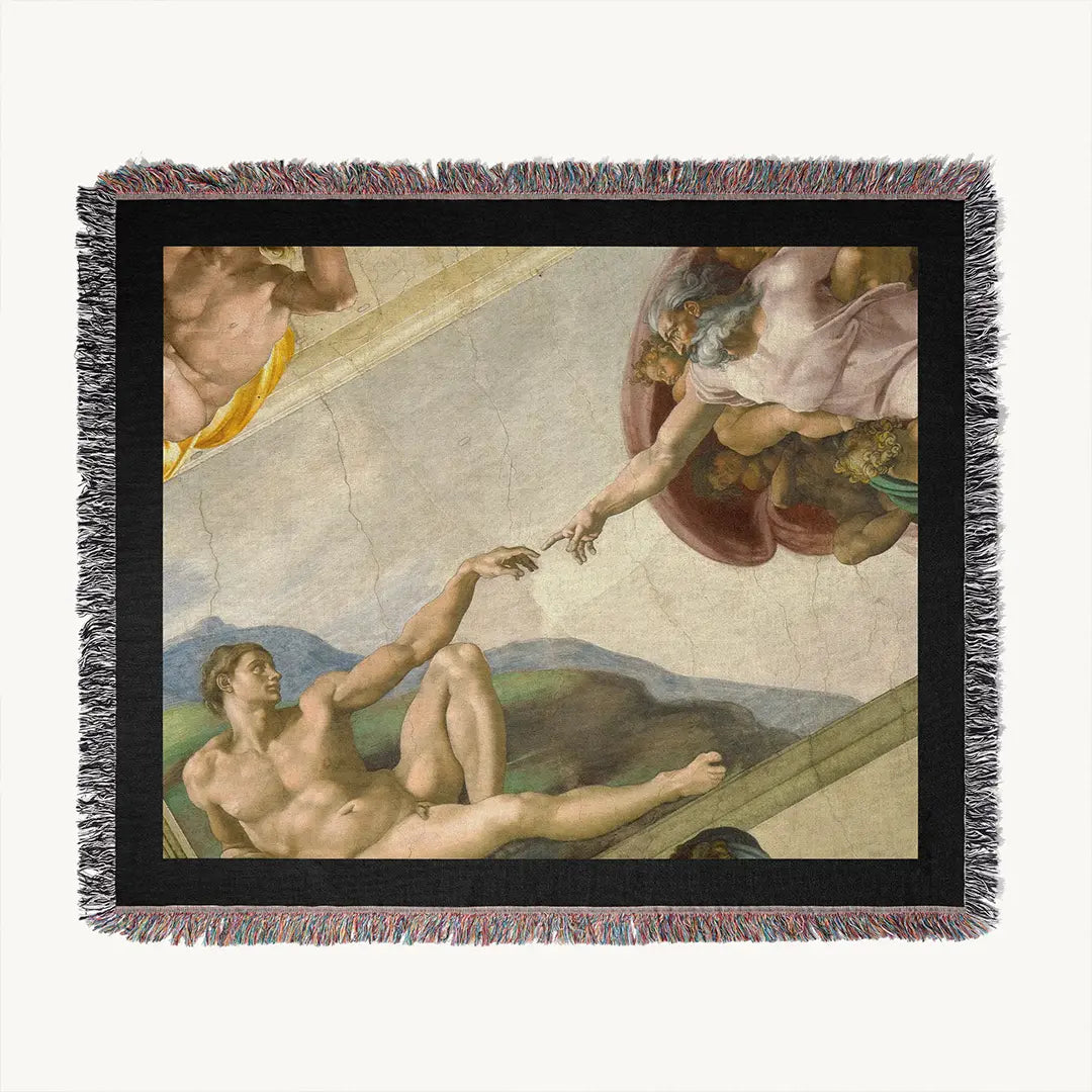Flat-lay of woven blanket with black border and fringe, featuring The Creation of Adam by Michelangelo on a white backround surface.