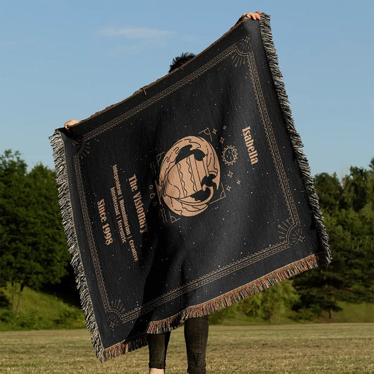 Outdoor view of an Aquarius-themed custom woven cotton blanket being held up under the blue sky, showcasing intricate zodiac artwork and traits.