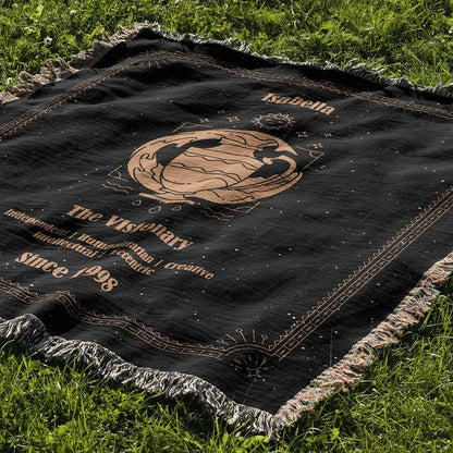 Black Aquarius zodiac-style custom woven cotton blanket laid out on a sunlit green lawn, displaying personalized name and traits.