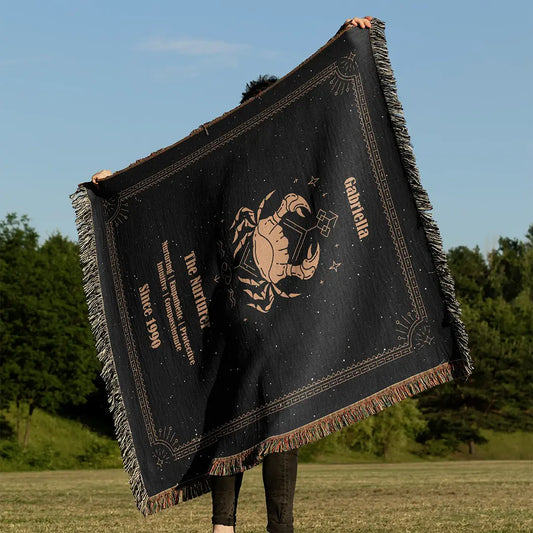 Custom woven cotton blanket featuring a Cancer Zodiac design held up against a clear blue sky in a grassy field.