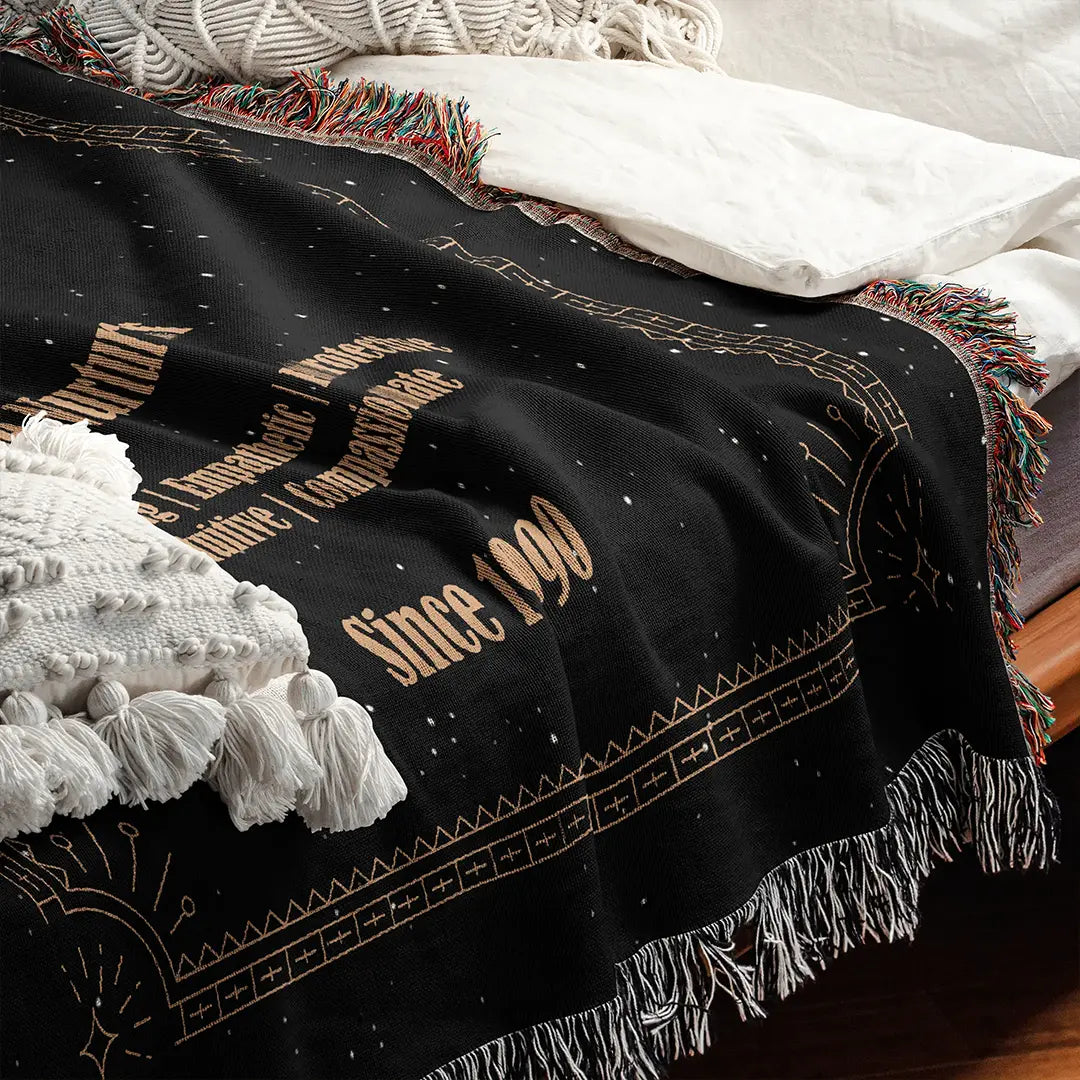 Custom woven cotton blanket with a Cancer Zodiac design draped on a bed beside white pillows and textured cushions.
