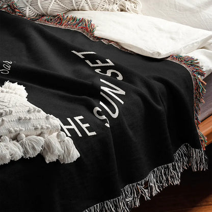A close-up of a custom woven cotton name blanket for couples on a bed, showing the soft texture, woven white typography, and detailed multicolor fringe edges.