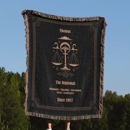Person holding a Libra zodiac custom woven cotton blanket outdoors in front of a clear blue sky and green trees.