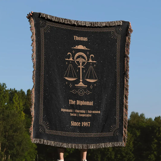 Person holding a Libra zodiac custom woven cotton blanket outdoors in front of a clear blue sky and green trees.