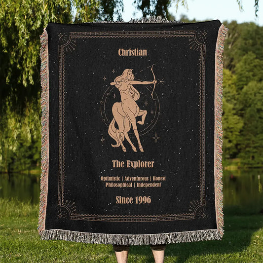 Custom woven cotton blanket held outdoors, showcasing a Sagittarius design in warm golden thread on a starry black background.
